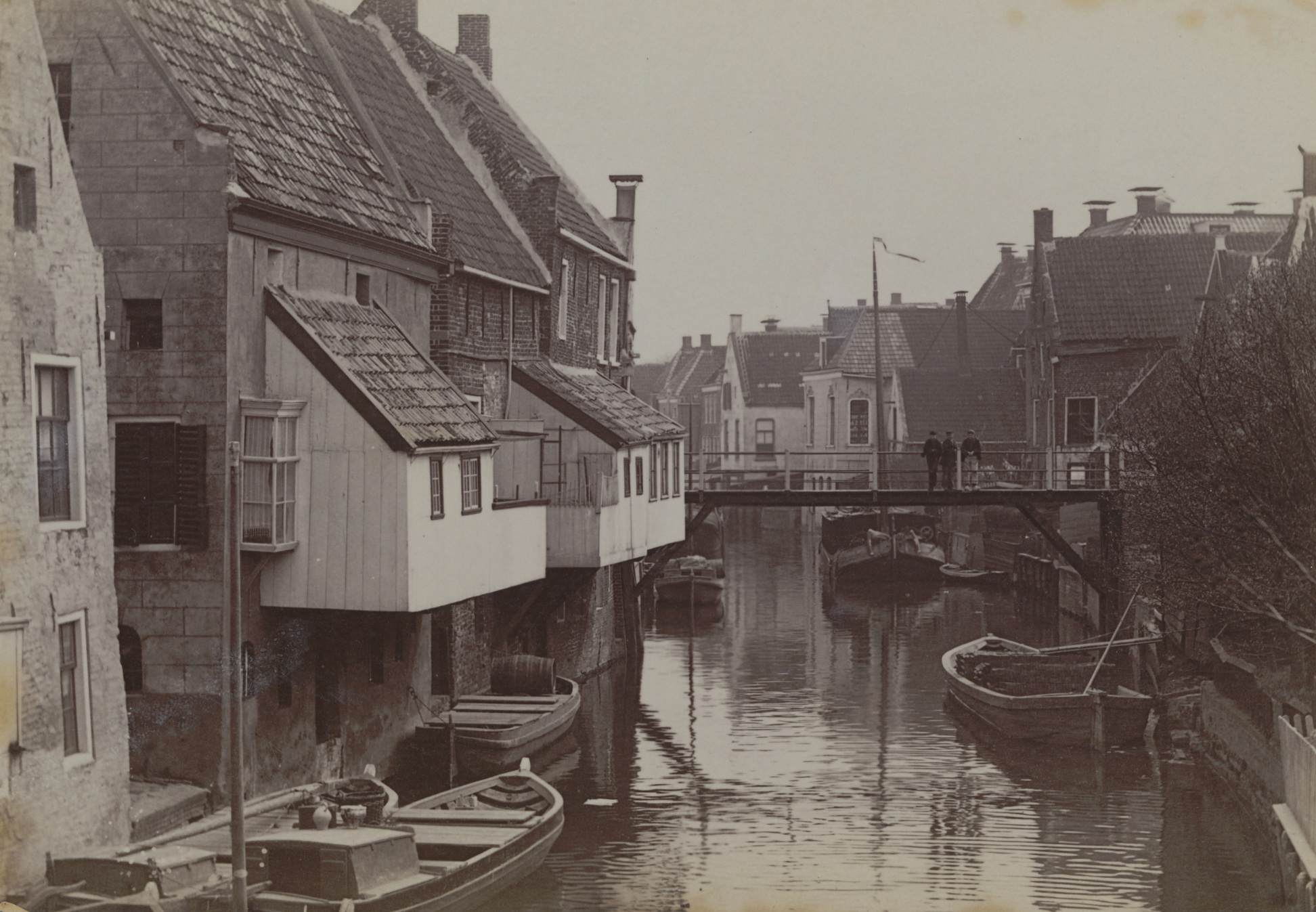 Damsterdiep in Appingedam. Damsterdiep met hangende keukens en op de achtergrond de Vrouwenbrug. Mogelijk uitgegeven als prentbriefkaart door La Rivière & Voorhoeve, Zwolle Verso in rood: 20. In potlood: Hoogezand; gemaakt tussen 1905 en 1915.